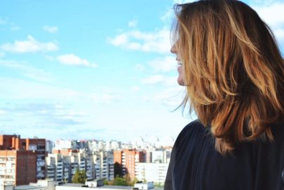 A woman standing on a rooftop, gazing over Saint Petersburg's urban skyline on a clear, sunny day.