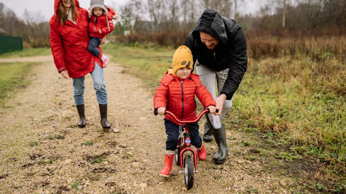 Happy family walking outdoors in fall, teaching child to ride bike.