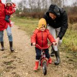 Happy family walking outdoors in fall, teaching child to ride bike.