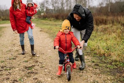 Happy family walking outdoors in fall, teaching child to ride bike.
