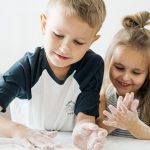 Two happy children enjoying baking, covered in flour while preparing dough at home.