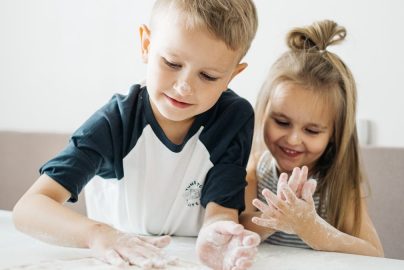 Two happy children enjoying baking, covered in flour while preparing dough at home.