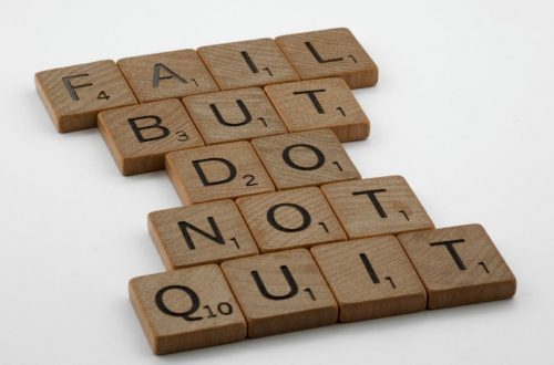 Close-up of Scrabble tiles forming the motivational phrase 'Fail but do not quit' on a white surface.